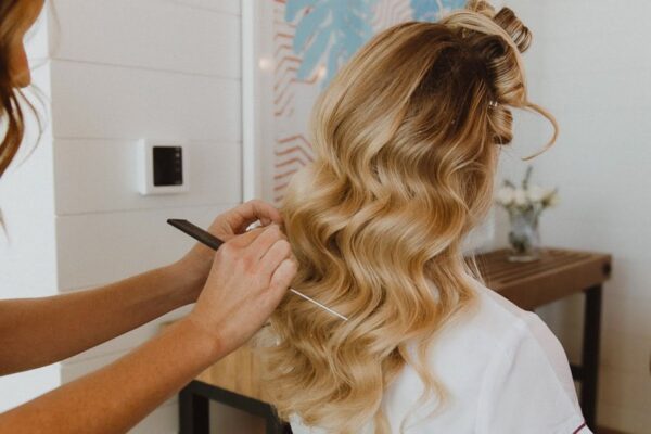 A bride receives a sophisticated hairstyle from a professional stylist, exemplifying wedding hair and makeup services. The focus on detailed styling showcases the meticulous work that goes into creating a picture-perfect look, hinting at the intricacy and expertise factored into wedding hair and makeup costs.